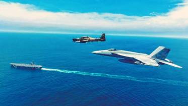 Un avi�n apoyo a�reo Embraer A 29 Super Tucano del Grupo de Caza 23 de la FAE vuela en formaci�n con un caza polivalente Boeing F/A-18E Super Hornet del  VFA 137 �Kestrels", en el fondo el portaaviones USS Nimitz (CVN 68). (Cr�ditos: SOUTHCOM)